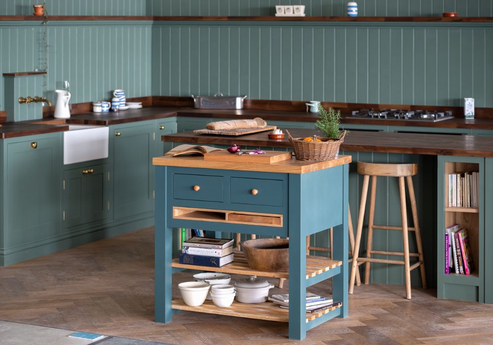 A neat small kitchen design with a teal island, wooden countertops, and shelves stocked with books and dishes.