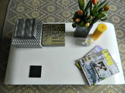 A white coffee table with magazines and flowers on it, featuring a contemporary dwell aesthetic.