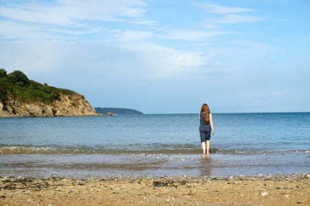 A woman is standing in the water on a beach, enjoying one of the 50 things to do recommended by the National Trust.