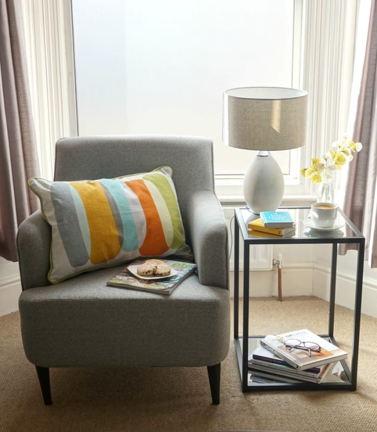 A grey chair in front of a window, creating a cozy reading corner.