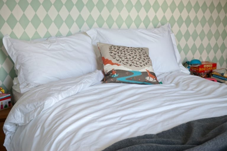A cozy bed in a room with beautifully patterned wallpaper.