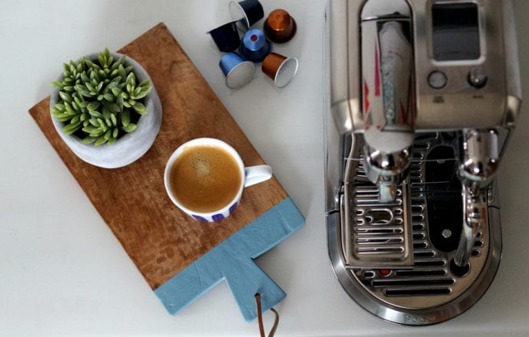 A Nespresso coffee machine with a cup of coffee on a wooden cutting board.