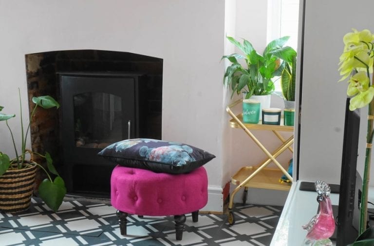 A living room with fabulous HomeSense furniture, featuring a fireplace and a pink ottoman.