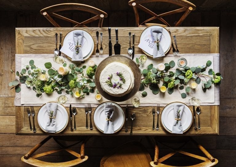 A wooden table set with greenery and place settings, bringing outside vibes indoors.