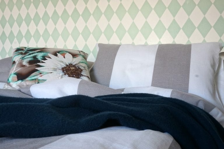 A guest bedroom with a bed adorned with pillows and a green and white striped wallpaper.