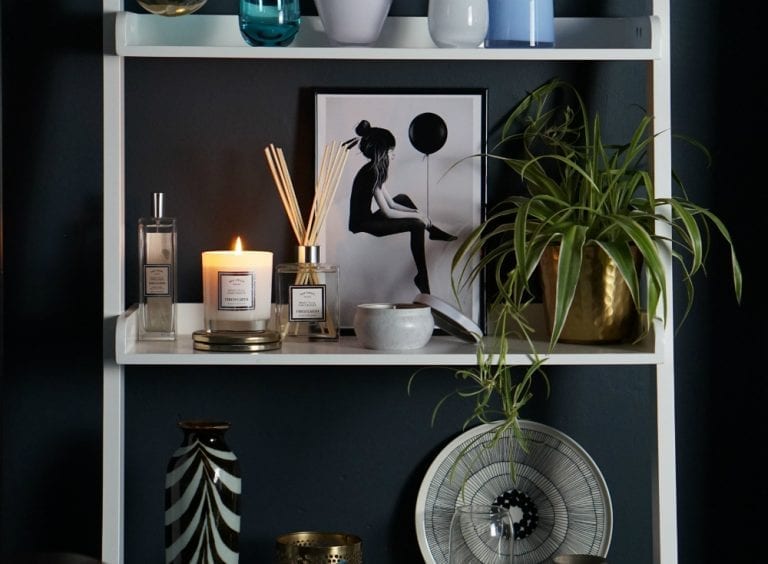 A shelf with Fired Earth Home Fragrance candles, vases, and a plant on it.