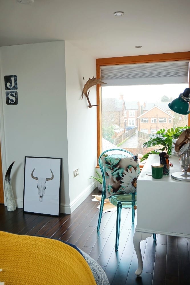 A completed loft conversion showing large window wooden floor, dressing table and yellow blanket on the bed