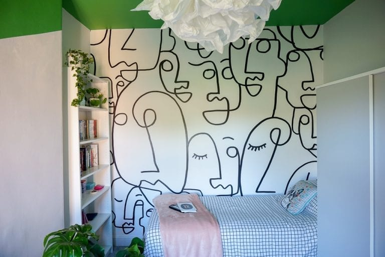 A teen girl's bedroom with a green wall and a white bed.