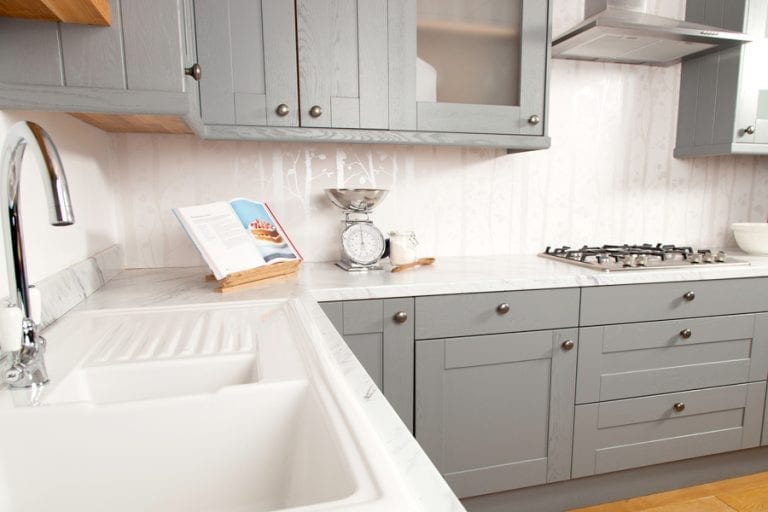A kitchen with grey cabinets and a white sink featuring a sleek kitchen worktop.