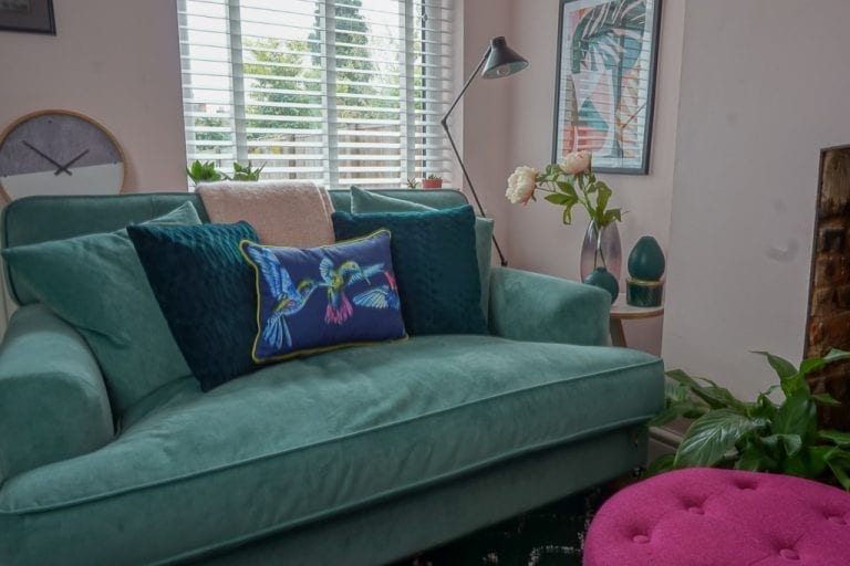 A cosy living room with a turquoise couch and pink ottoman.