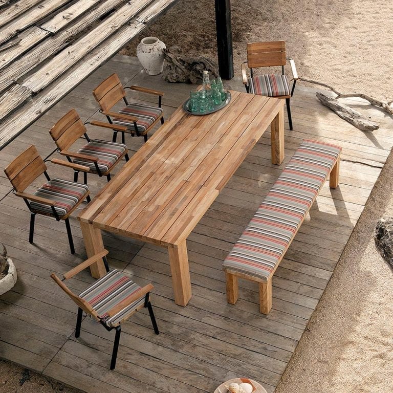 A wooden dining table and chairs on a wooden deck, made of garden furniture material.