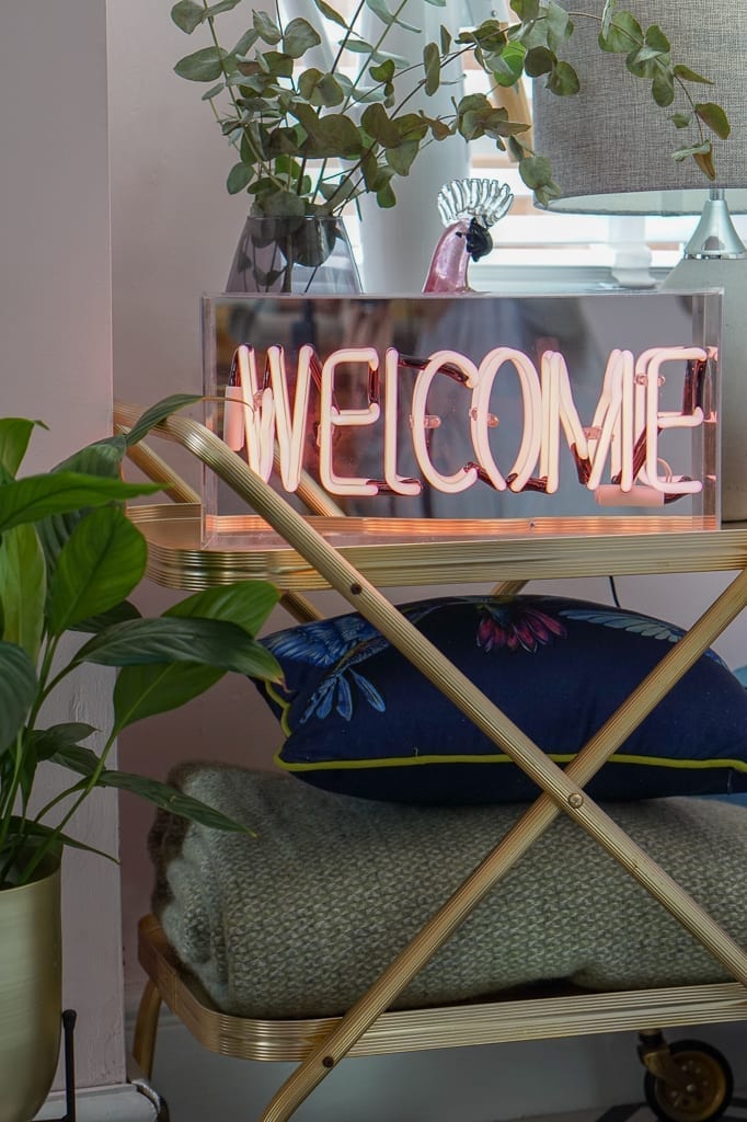 A neon welcome sign sits on a table in a living room, making it the perfect addition for any Home Lover.