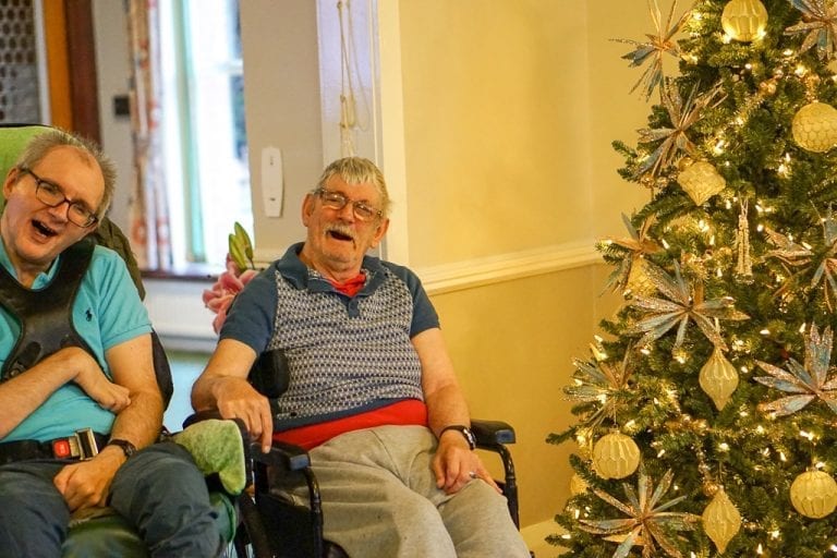 Two men in wheelchairs in front of a Christmas tree donated by Leonard Cheshire Charity.