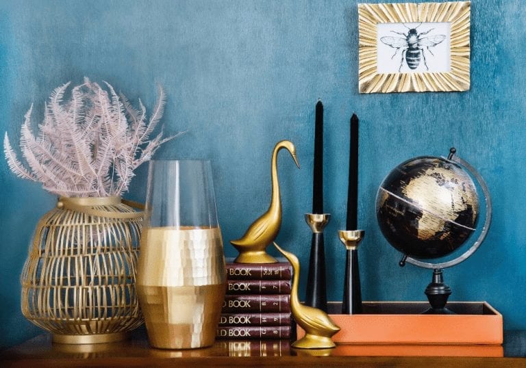 Gold vases, books, and a globe are displayed on a blue wall for a quick house sale.
