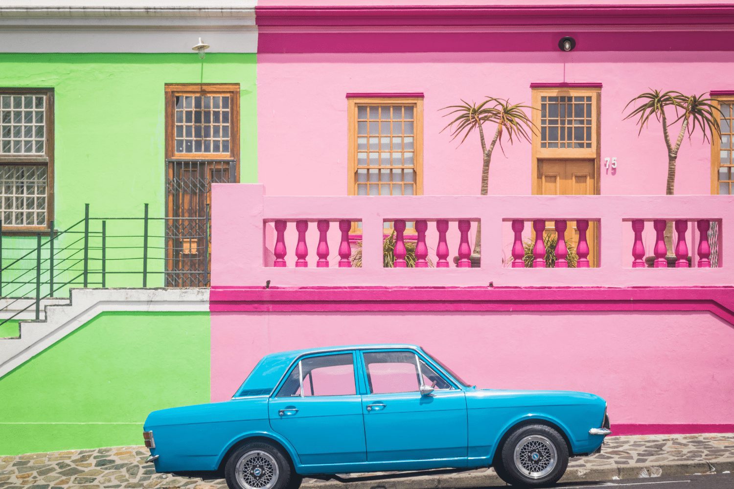 A blue car parked in front of a colorful house in Cape Town.