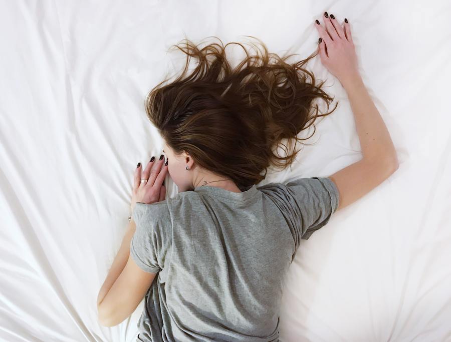 Woman lying face down on a white bed with her hair spread out, enjoying a good night's sleep.