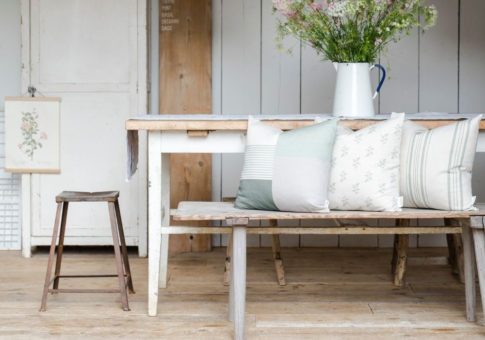Rustic wooden garden furniture bench with decorative pillows against a shabby chic backdrop.