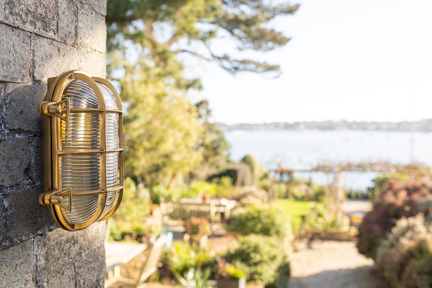 Wall-mounted outdoor elesi lighting with a view of a garden and water body in the background.
