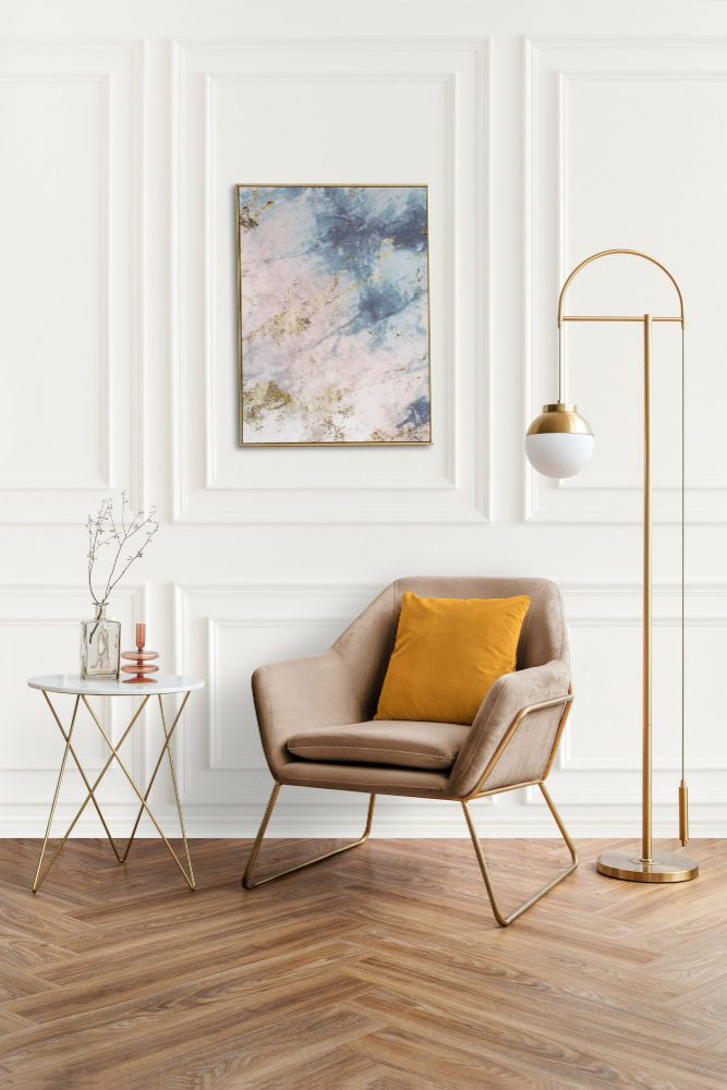 Elegant modern living space featuring a beige armchair with a yellow cushion, a brass floor lamp, and abstract wall art, embodying simple ways to brighten your home without wasting money.