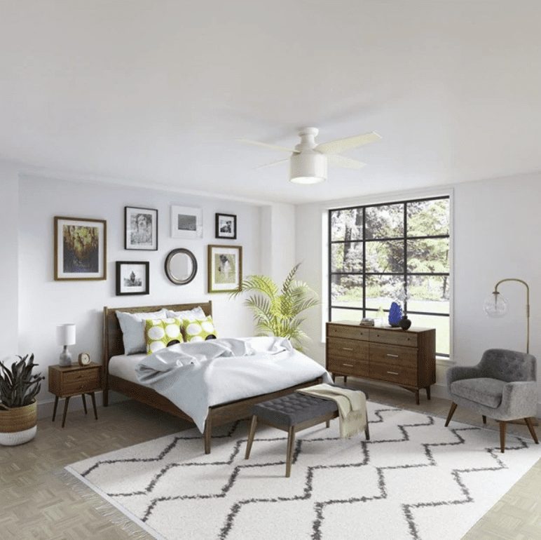 Modern bedroom with neutral colors, contemporary furniture, and a ceiling fan, showcasing a view of trees outside the window.