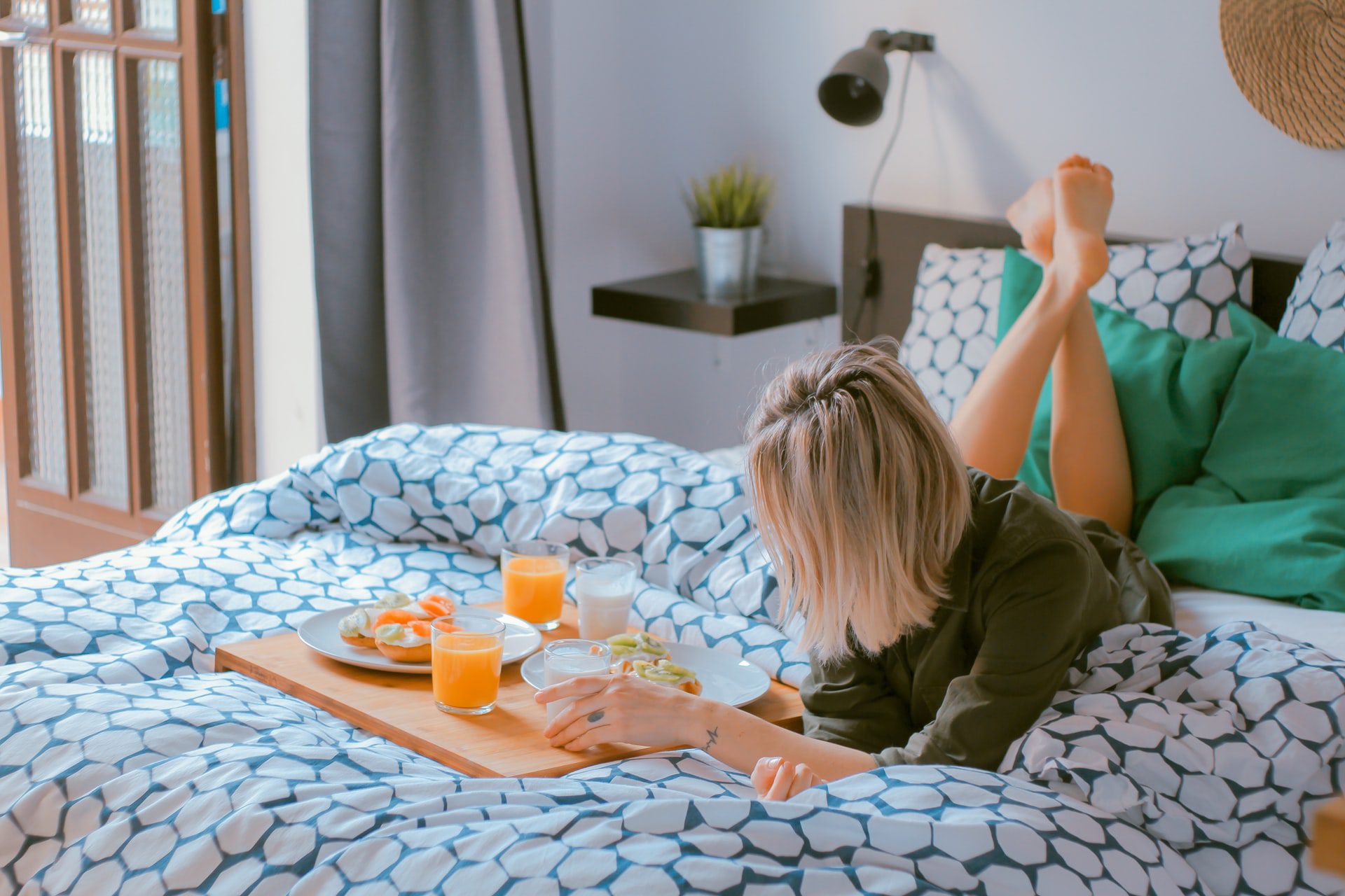 A person relaxing on an Alaskan king bed with a tray of breakfast items.