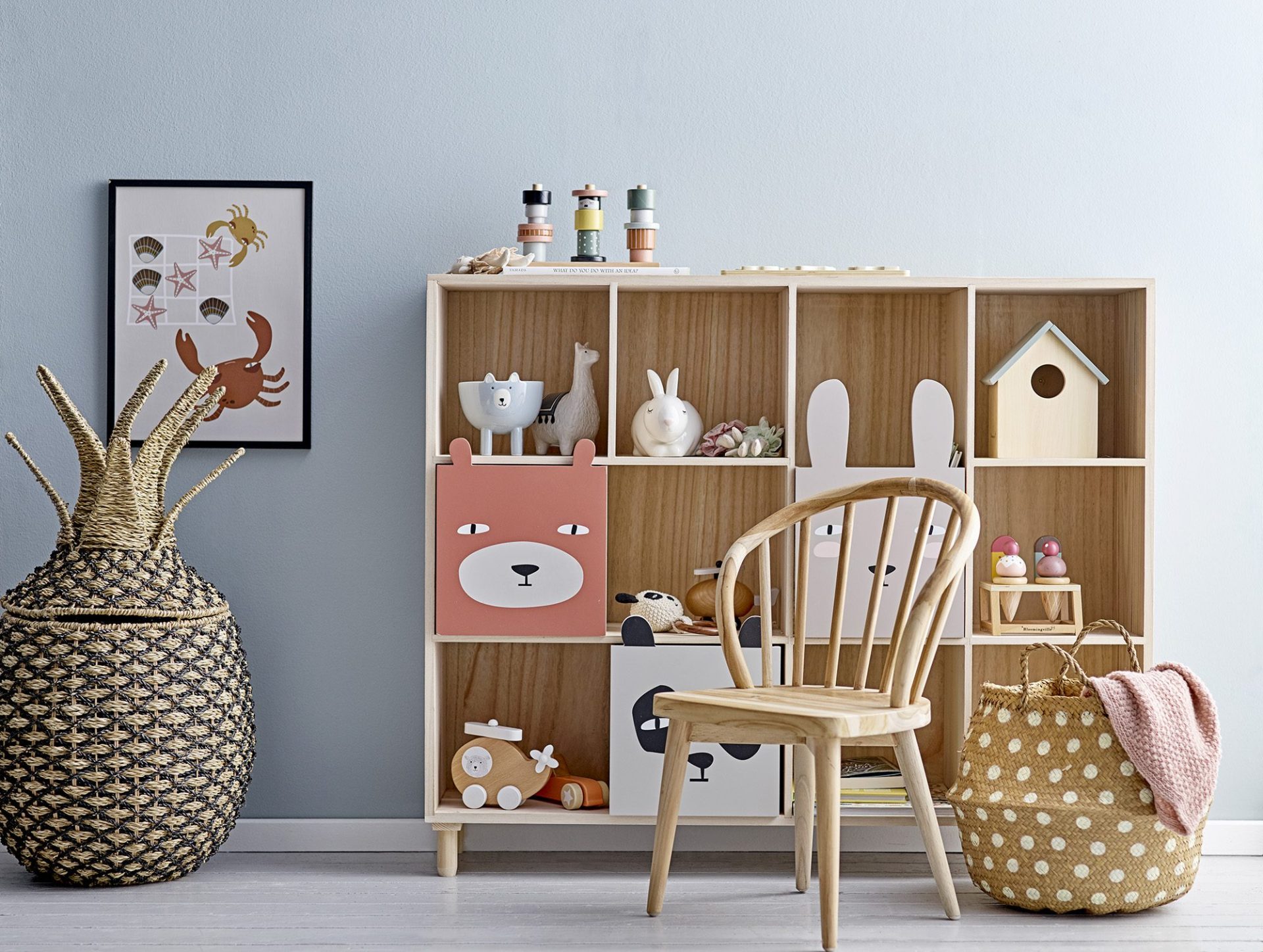 Scandinavian-style kid's play space with a wooden storage unit displaying toys and a cozy chair beside a wicker basket.