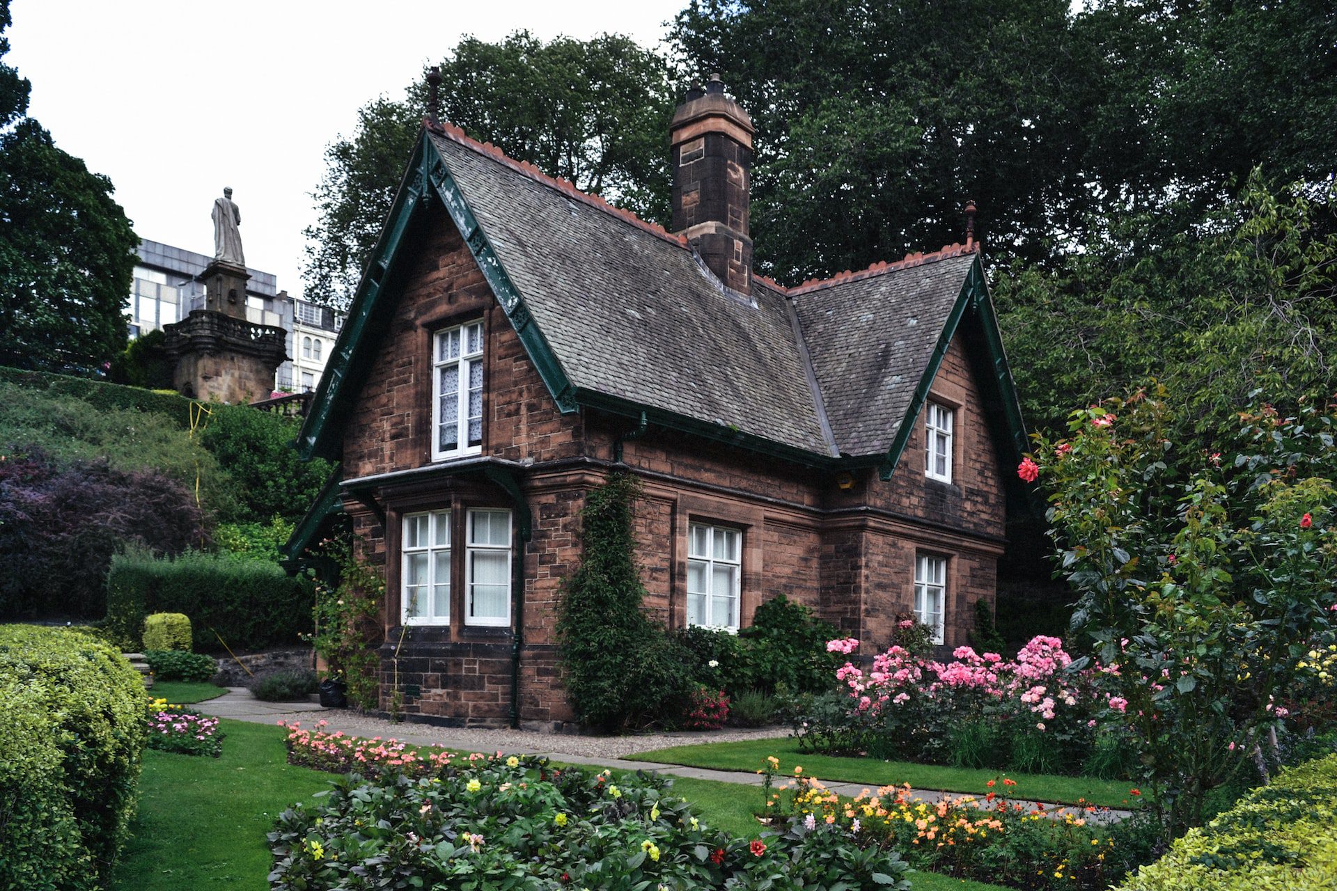 Traditional brick house with a tired exterior, surrounded by manicured gardens and blooming flowers, set against a background of lush green foliage.