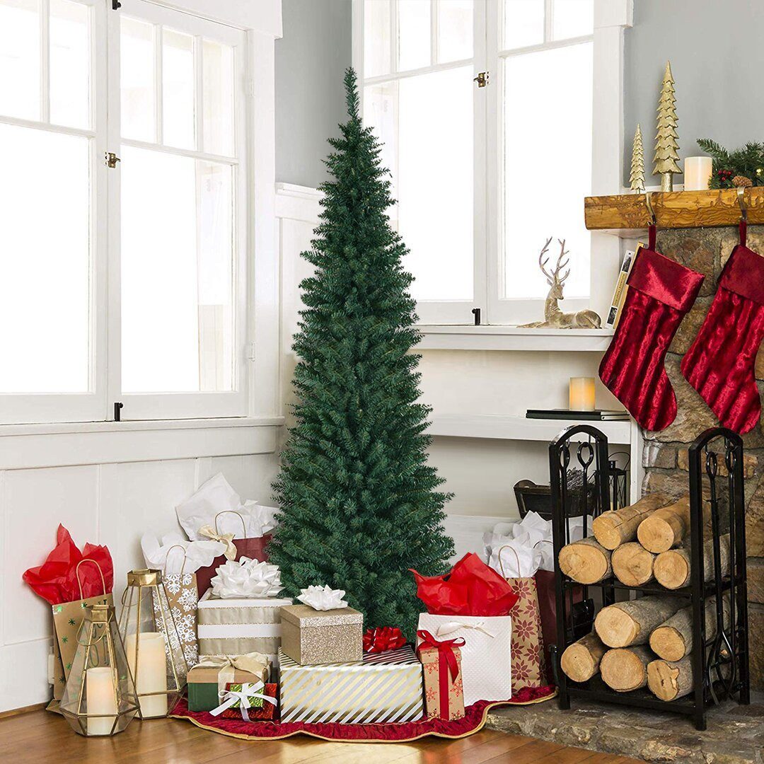 Green slim Christmas tree in small home surrounded by gold wrapped Christmas gifts