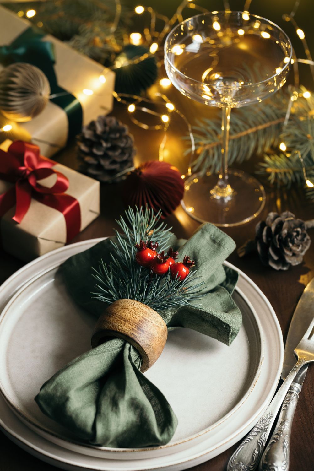 A festive table setting featuring a napkin ring with greenery on stacked plates, surrounded by holiday decorations, gifts, and a glass of wine, all arranged for a stress-free Christmas.