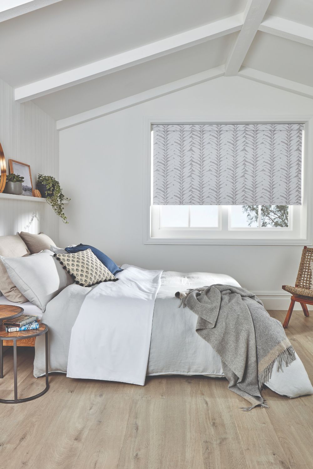An attic converted to a spare bedroom with neutral blind, wooden floor, double bed with white and grey bedding