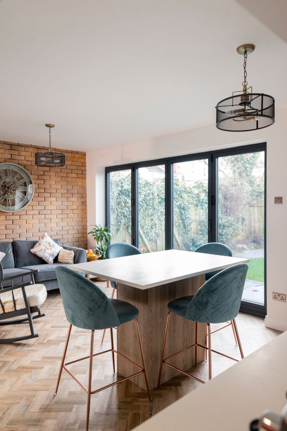 Modern dining room with a wooden table, teal chairs, exposed brick wall, and large windows overlooking a garden, perfect for those considering a home upgrade.
