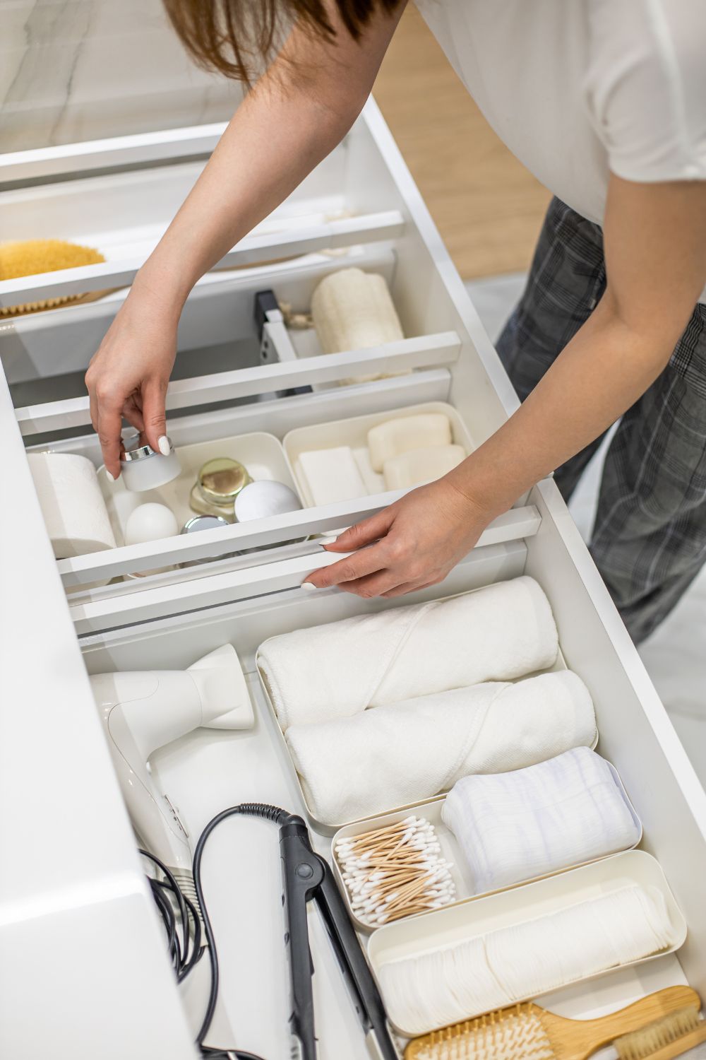 A woman organizes various bathroom items in a white, segmented storage drawer to avoid moving mistakes.