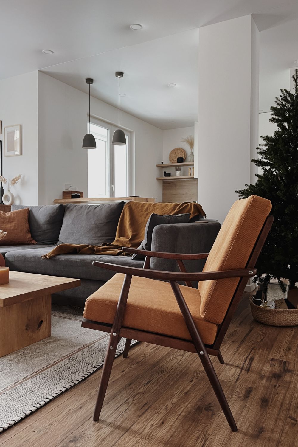 Modern living room featuring a gray sofa, orange armchair, wooden coffee table, and a Christmas tree in the corner, designed with contemporary interior design principles.