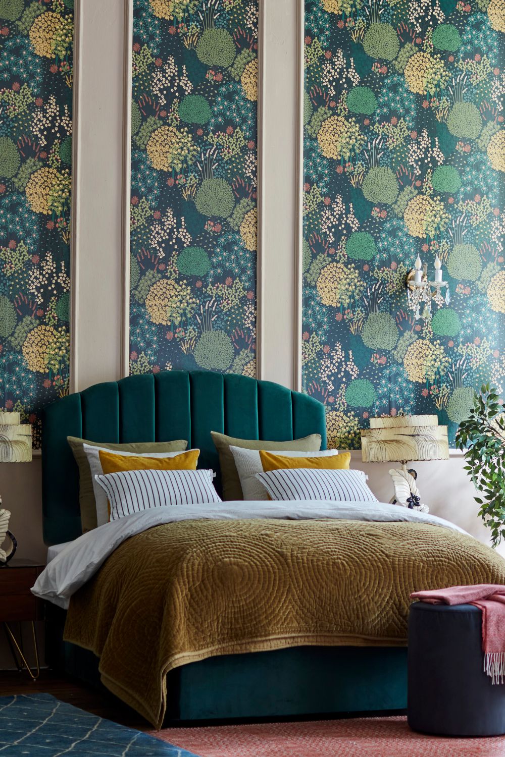 A stylish bedroom featuring a teal upholstered bed with green and gold bedding, set against a vibrant floral wallpaper and accessorized with yellow pillows, aligns perfectly with 2023 bedroom trends.