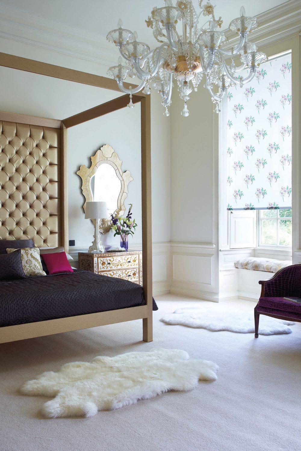 Elegant bedroom interior with a large canopy bed, intricate chandelier, and floral wallpaper, featuring plush white rugs and a window seat.