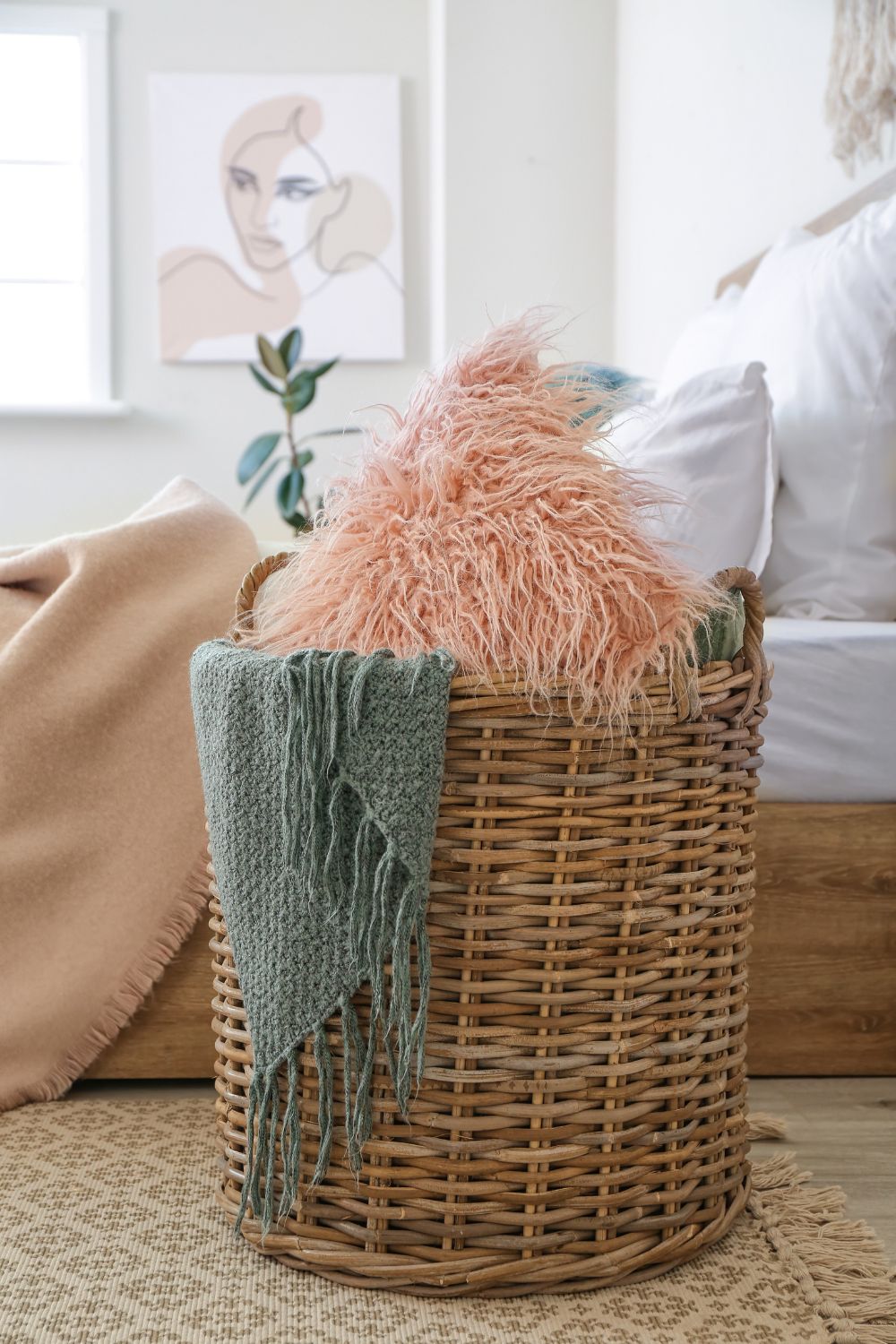 Light bedroom with wicker basket for storage of pink cushion and grey blanket with white bed in the background