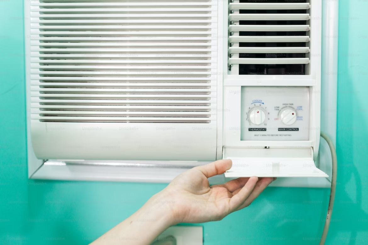 A person’s hand adjusting the dials on a wall-mounted air conditioner unit with the best air conditioning filter against a teal background.
