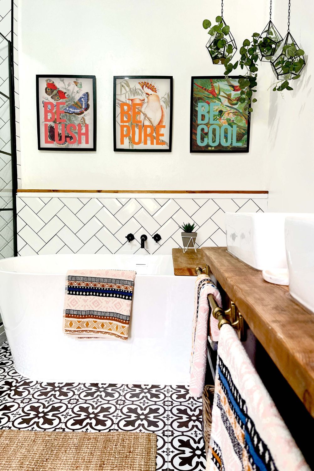 Modern bathroom featuring a white freestanding bathtub, geometric tiled floor, wooden countertop with damp control, and framed art on the wall.