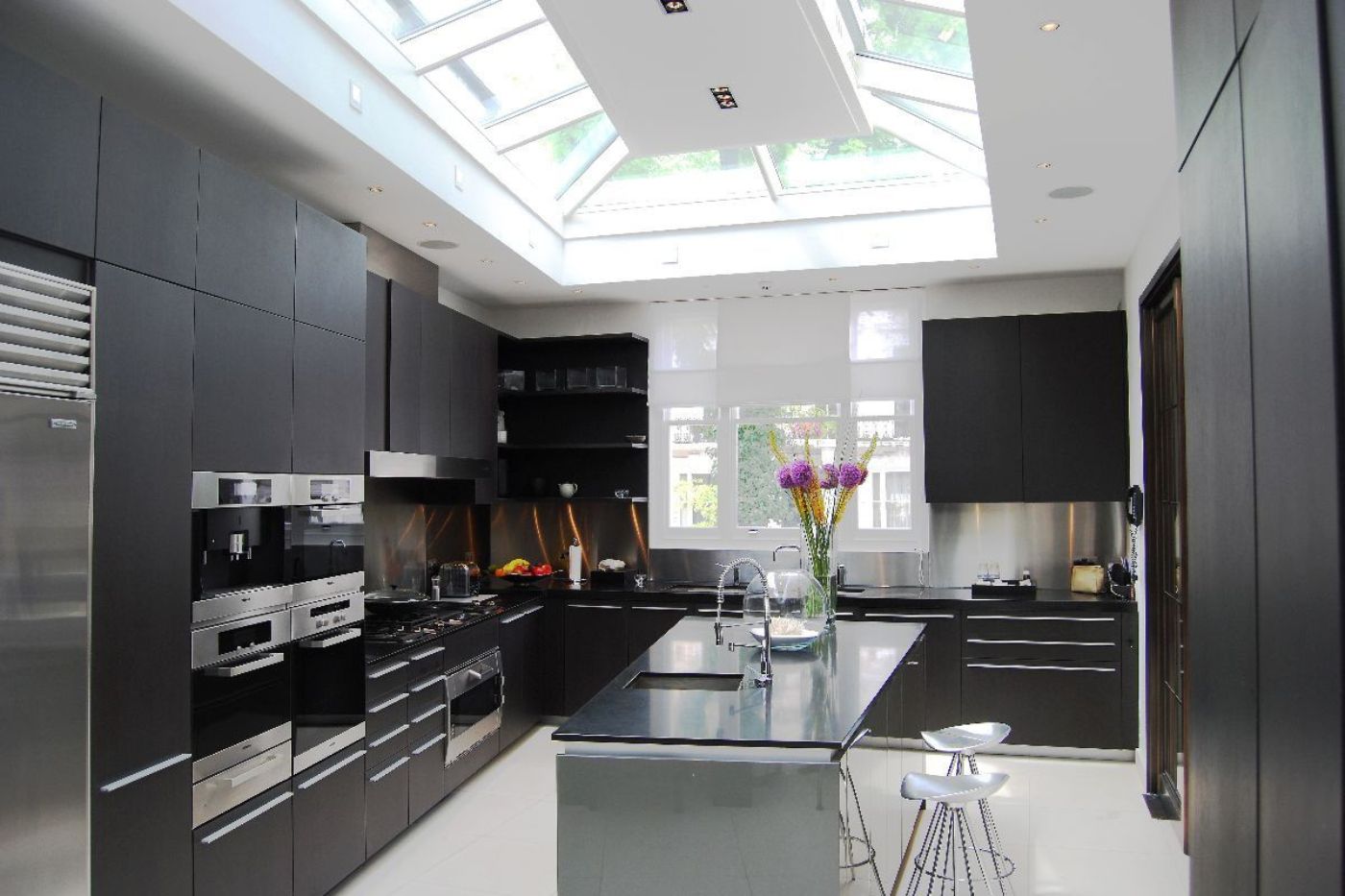 Modern home kitchen with black cabinets, central island, and skylights.