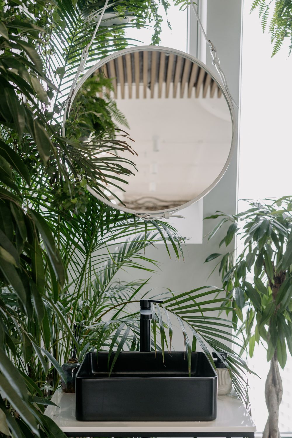A small boho bathroom with round mirror and lots of plants