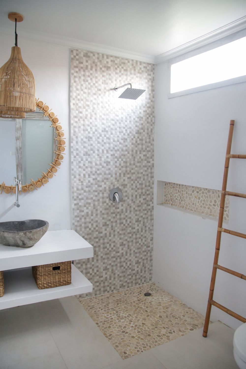 A simple boho bathroom with tiled shower area and wite walls with round stone sink