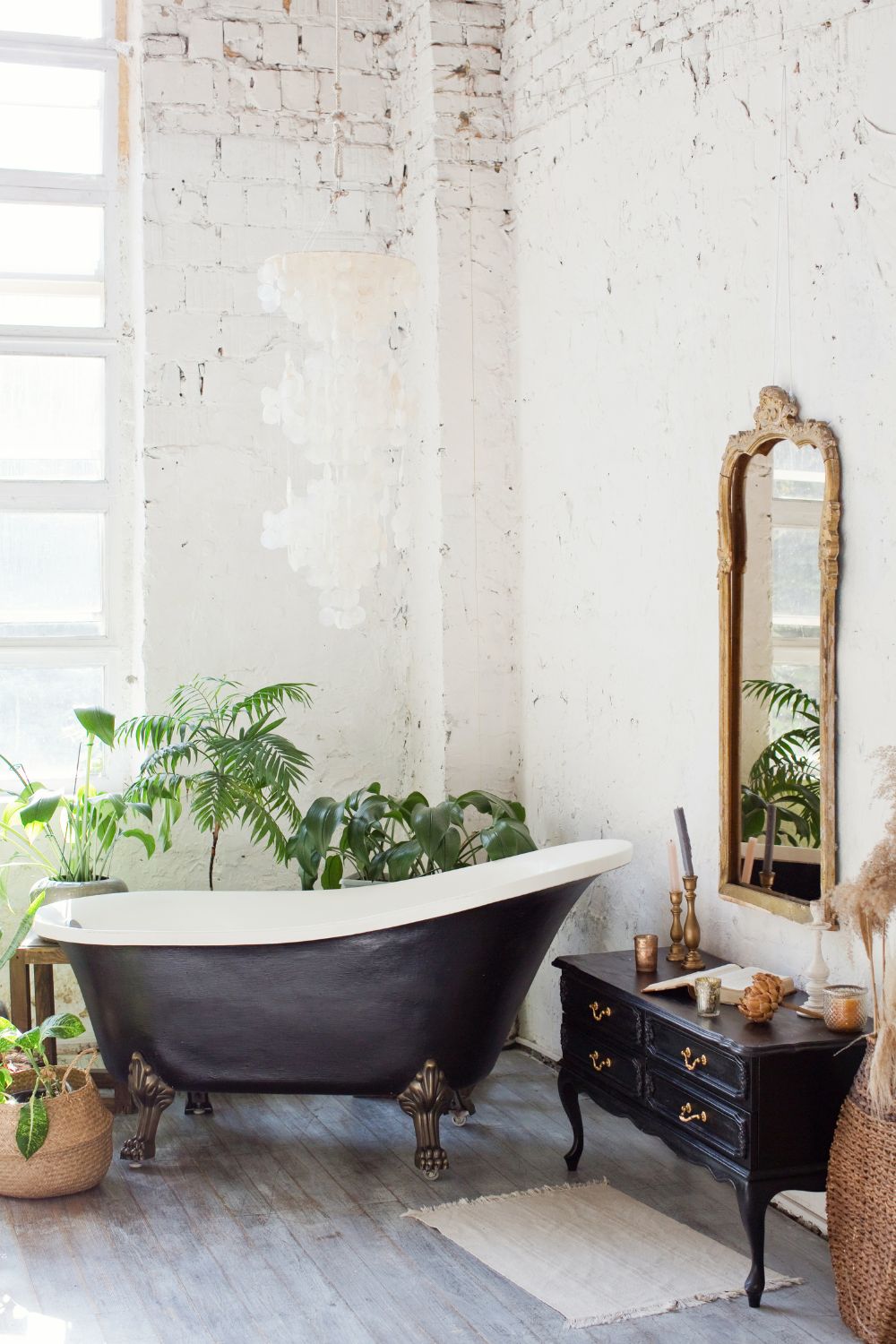 A large boho bathroom with white walls, a black standalone bath, gold mirror and lots of plants.