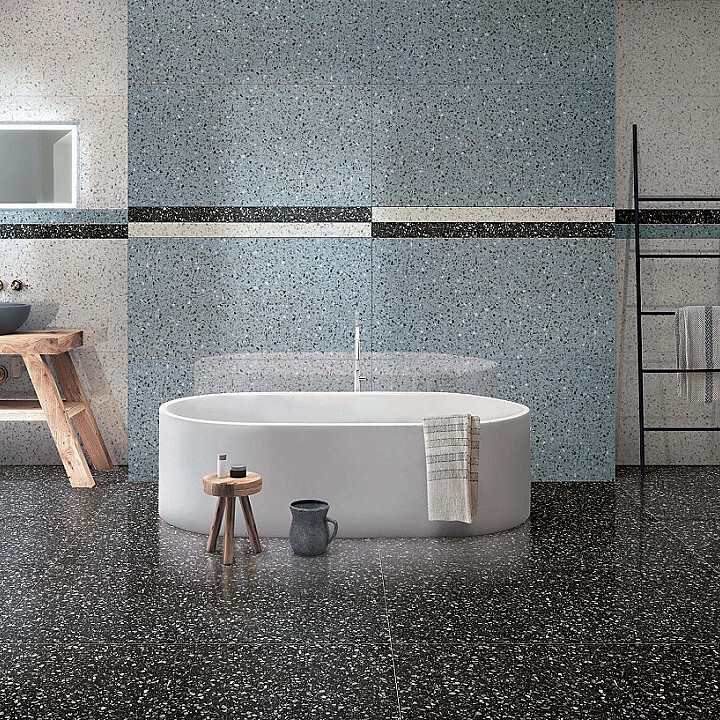 Modern bathroom featuring an innovative design with a white oval bathtub, terrazzo flooring, and a speckled blue wall, accompanied by a small wooden stool and black accessories.