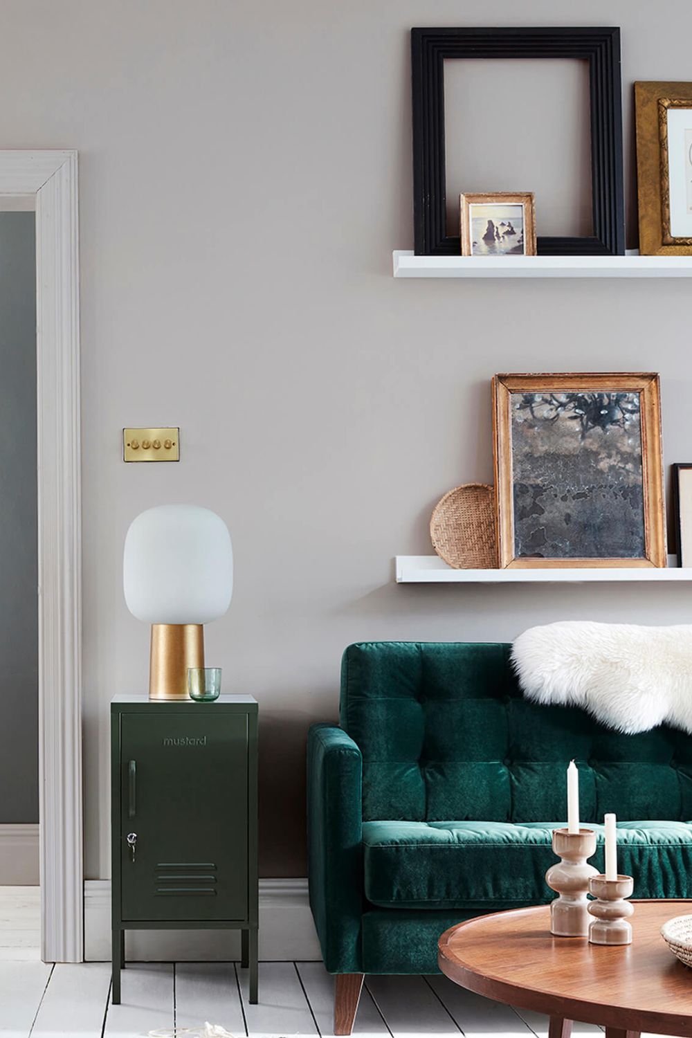 A cozy couch with a white fur blanket and a warm lamp on a shelf in a green living room.