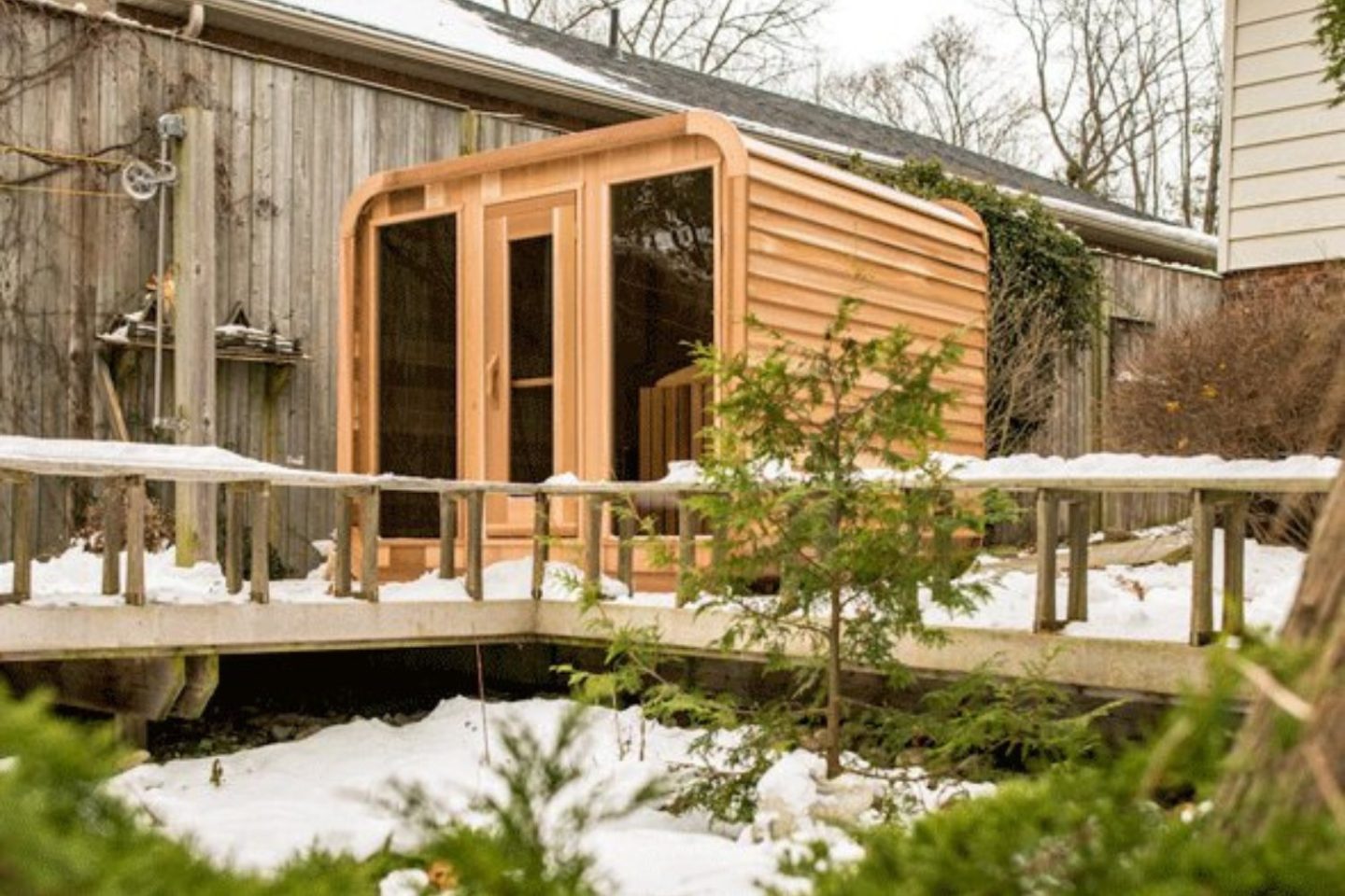 A custom wooden sauna in a backyard covered in snow.