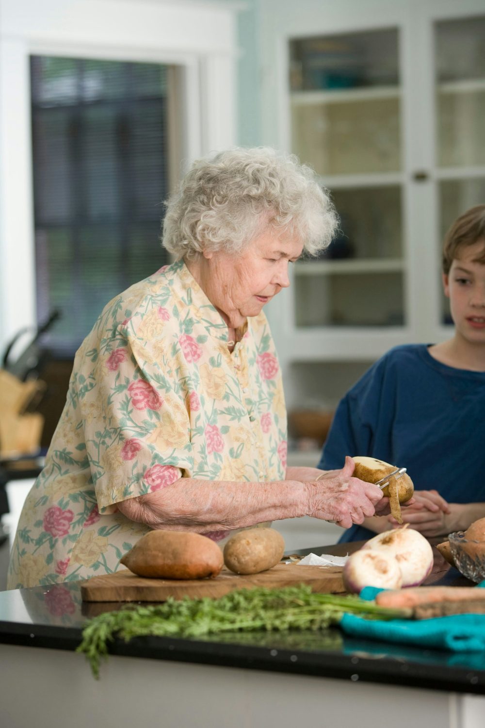 An older woman and a young boy preparing food in the kitchen of their house.