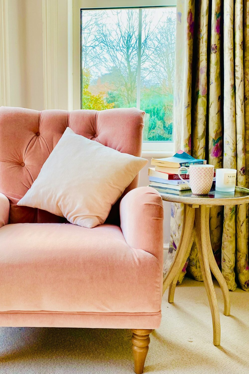 A pink velvet chair in front of a window in a house.