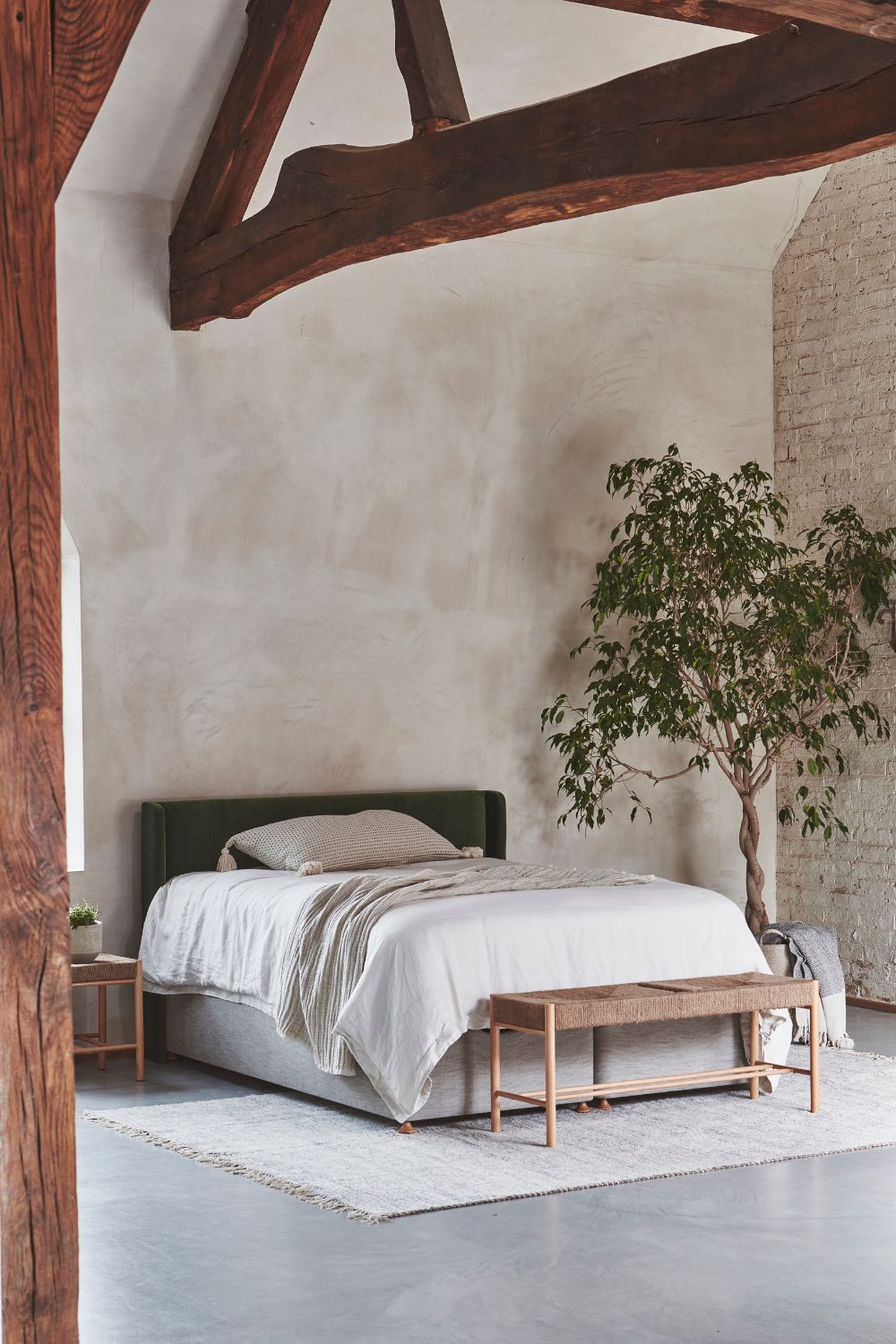 A minimalist, eco-friendly bedroom with a green headboard, exposed wooden beams, and a potted tree.