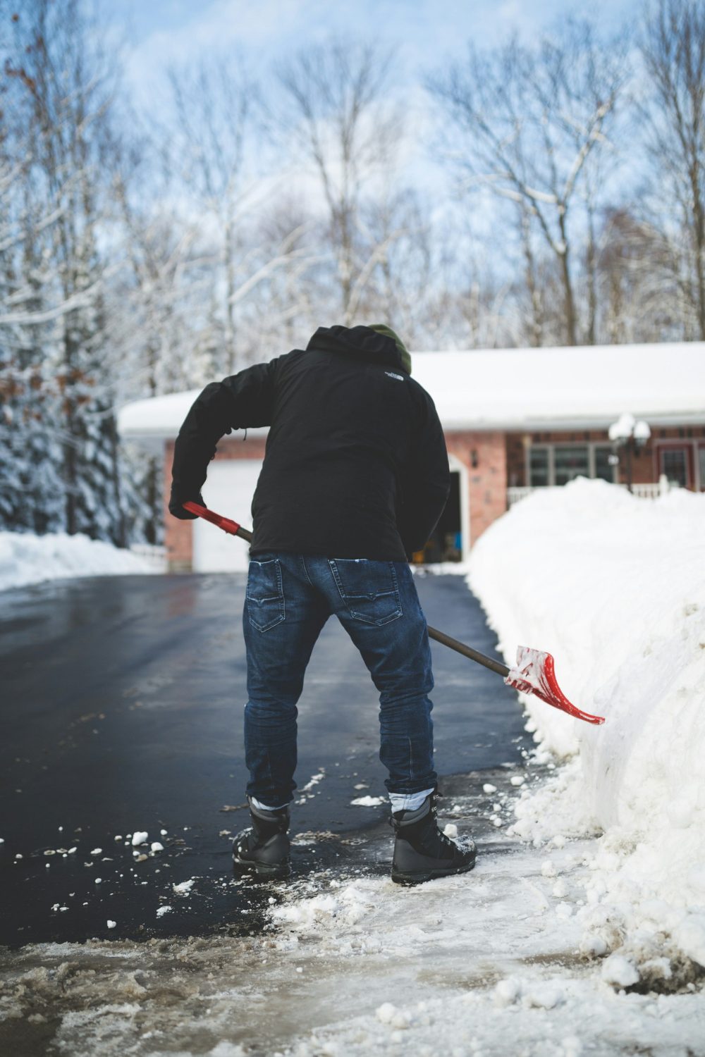 A man clearing snow from the walkway in front of a house using easy methods.