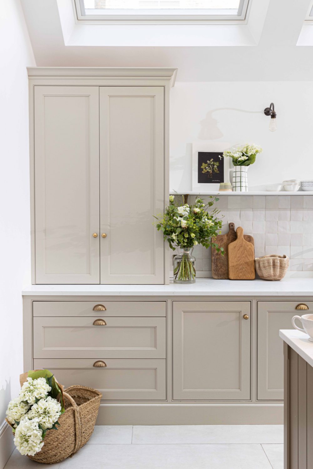 Elegant kitchen corner featuring beige cabinetry with gold element handles, a countertop with fresh flowers and cutting boards, and a basket of hydrangeas.